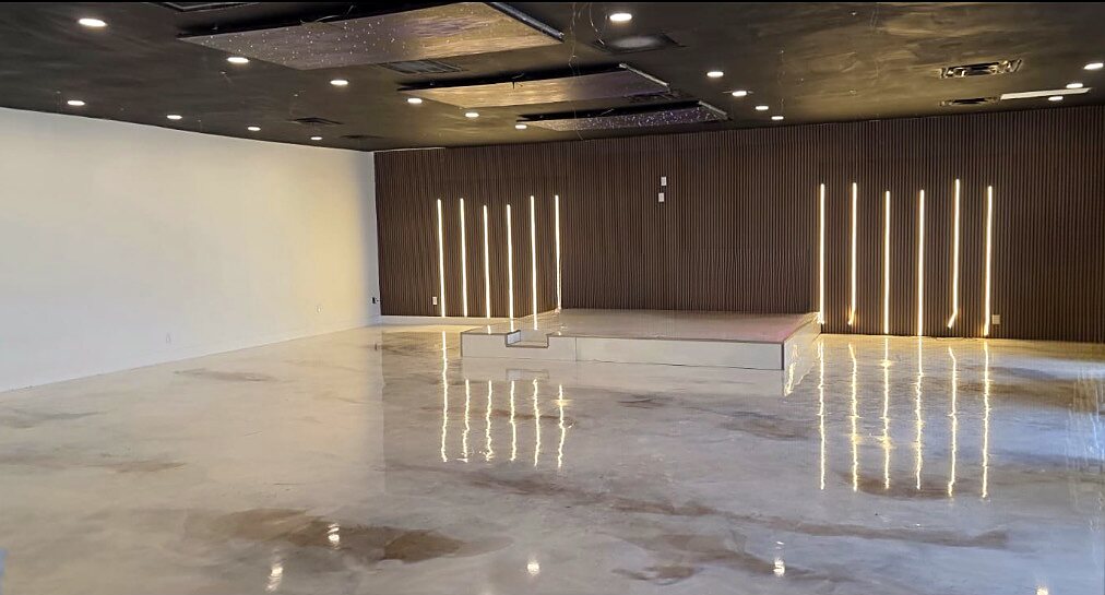 Event hall at La Belle Porte Venue with a low stage, lit wood-slat accent wall and glossy marble-look floor